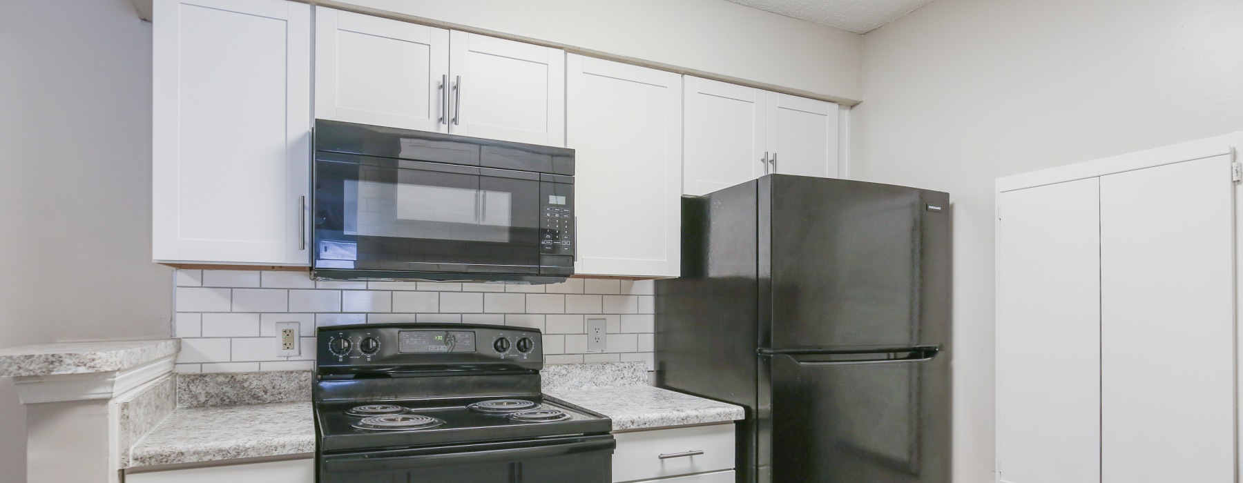 Apartment kitchen with white cabinets and black appliances