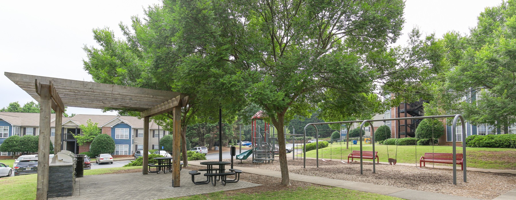 Grill and picnic area surrounded by trees near playground